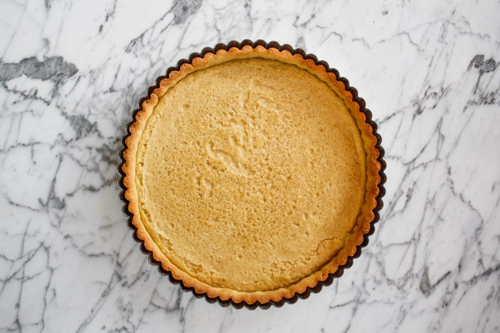 Tart pan lined with baked tart crust set on top of a marble surface.