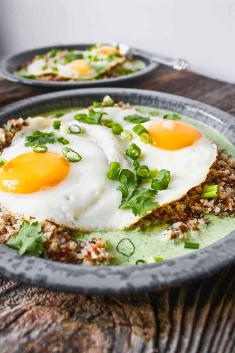 A gray metal plate with green sauce, grains, and sunny side up eggs, set on top of worn wood slabs.