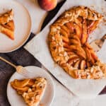 photo of a peach galette on a piece of parchment paper with slices on plates scattered around.