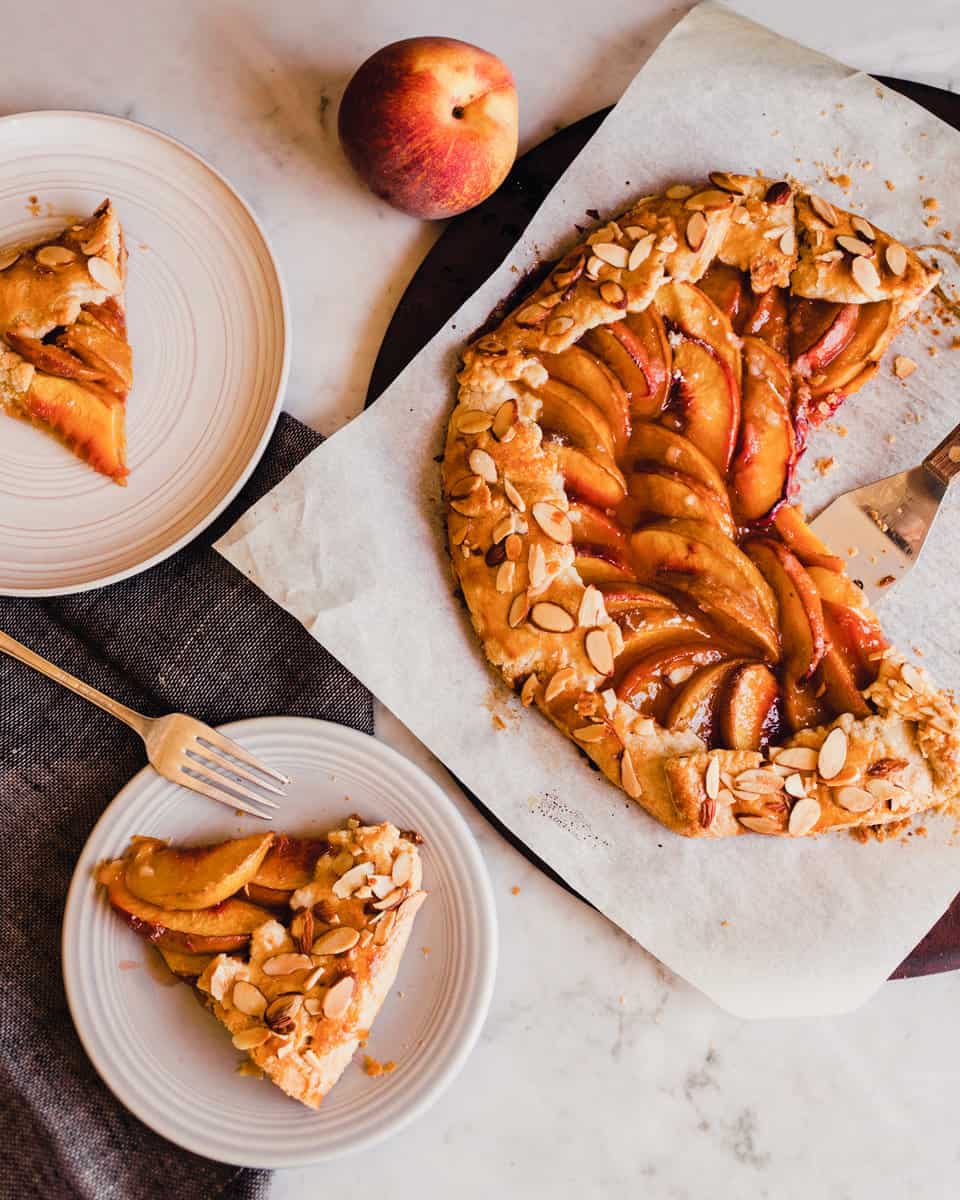 photo of a peach galette on a piece of parchment paper with slices on plates scattered around.