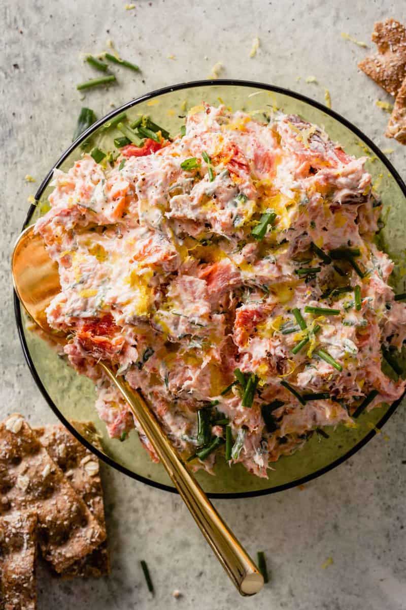 creamy salmon dip topped with herbs in a green glass bowl with a gold spoon set in it