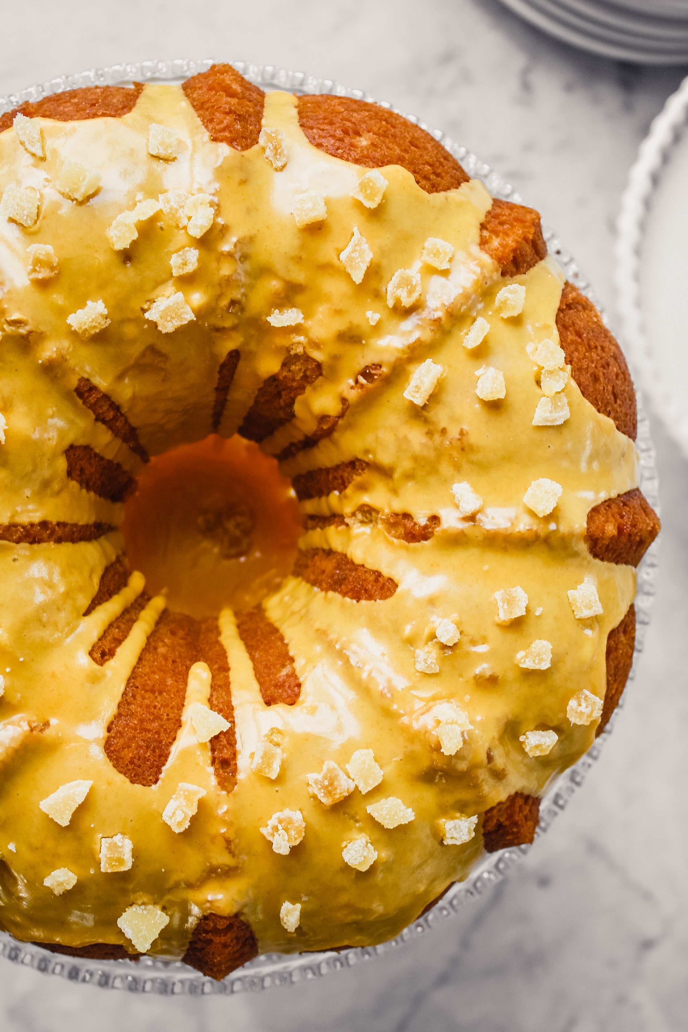 Photograph of orange and ginger bundt cake with turmeric glaze on glass cake stand