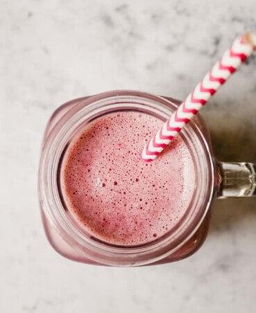 Photograph of a pink smoothie in a ball glass jar with a pink and white straw