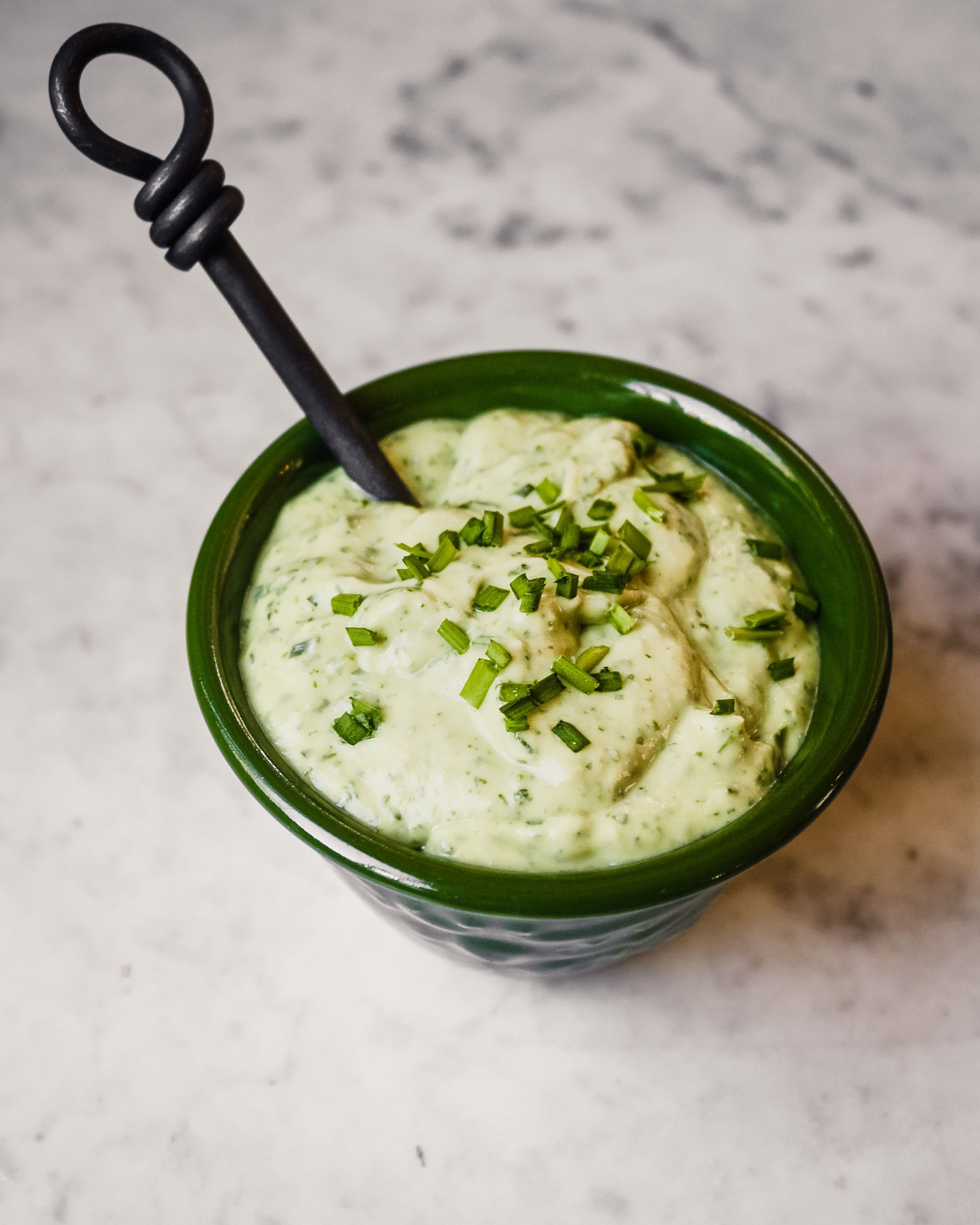 Photograph of a green bowl filled with green goddess dressing set on a marble table.