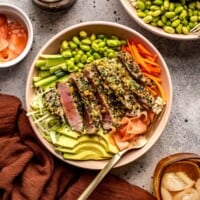 sliced crusted ahi tuna steaks in a bowl filled with fresh vegetables, rice and pickled ginger
