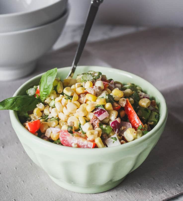 Photograph of corn salad in a green bowl set on a marble table.