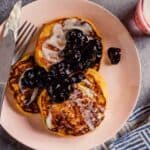yellow pancakes on a pink plate topped with blueberry sauce