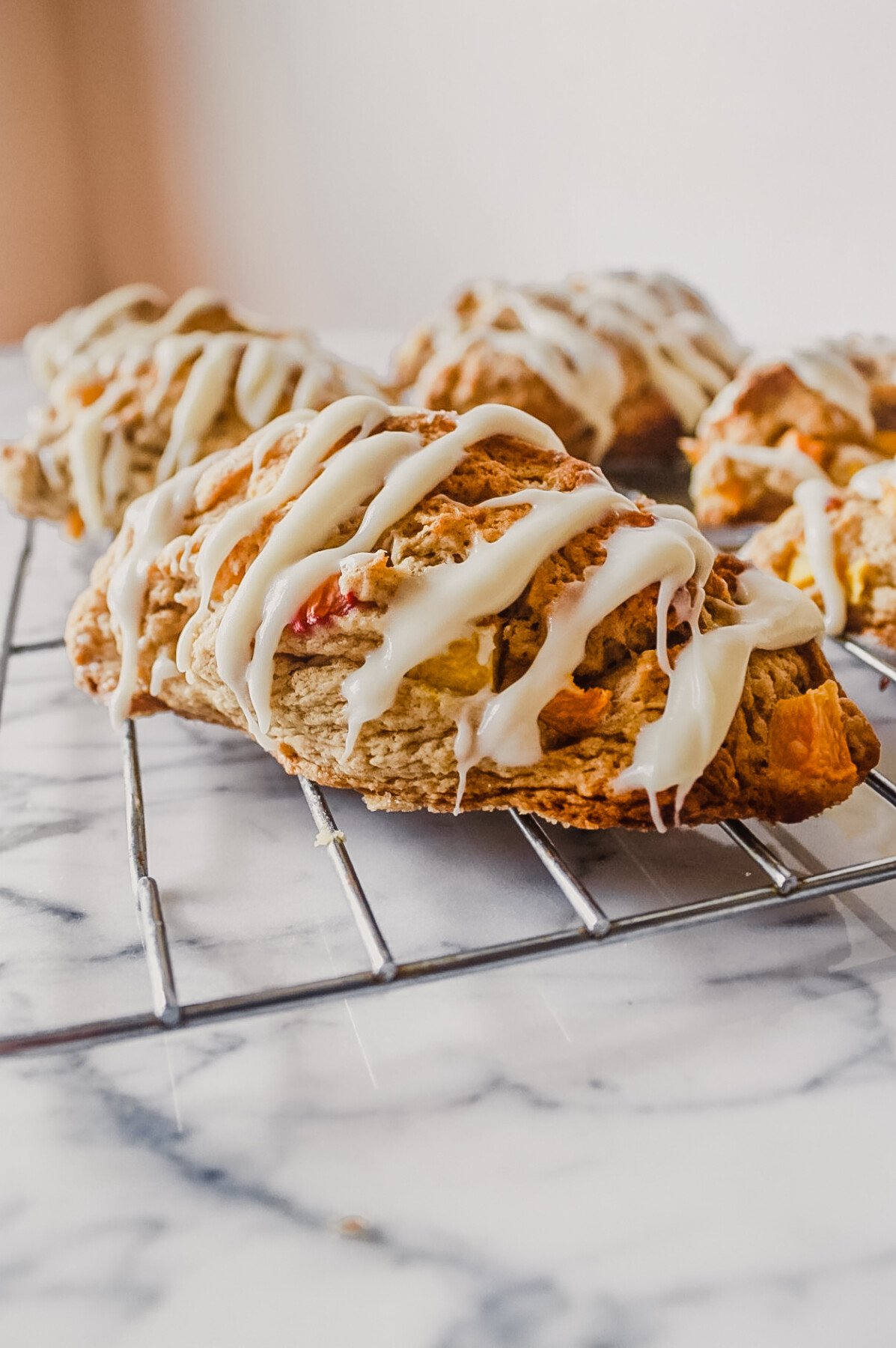 Peach scones with a cream cheese drizzle set on a wire rack