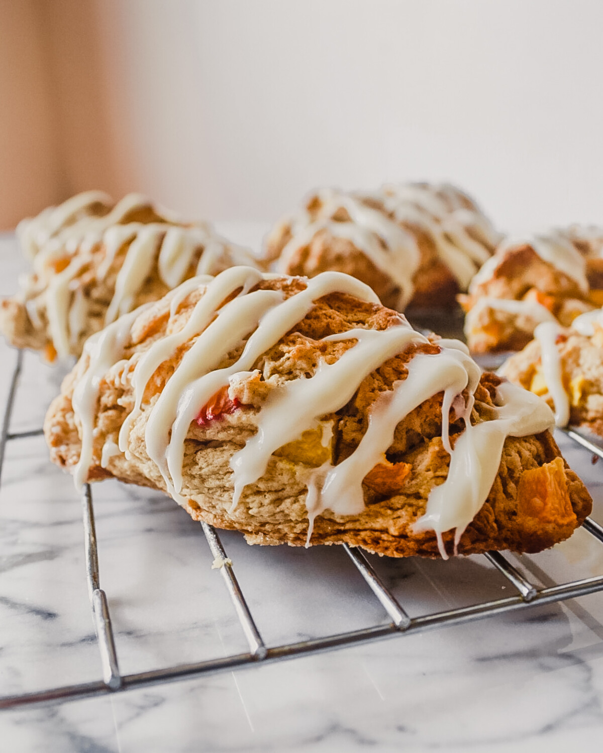 Peach scones with a cream cheese drizzle set on a wire rack