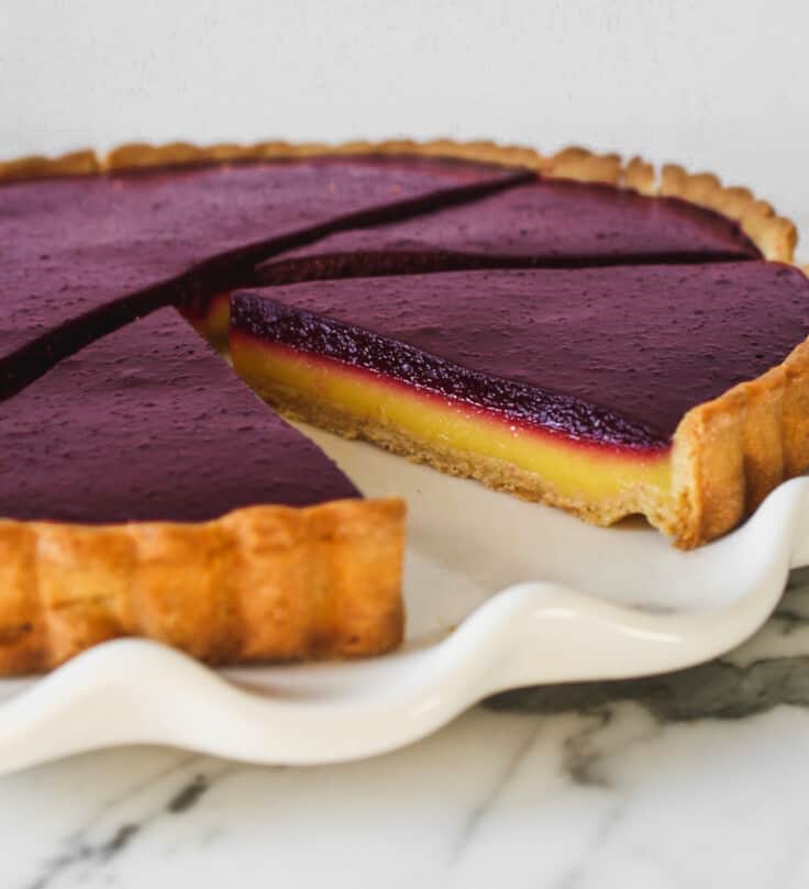 Tart slices, with yellow and purple layers, set on top of a marble surface.