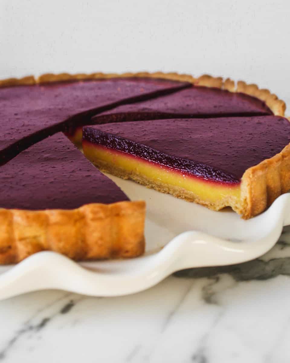 Tart slices, with yellow and purple layers, set on top of a marble surface.
