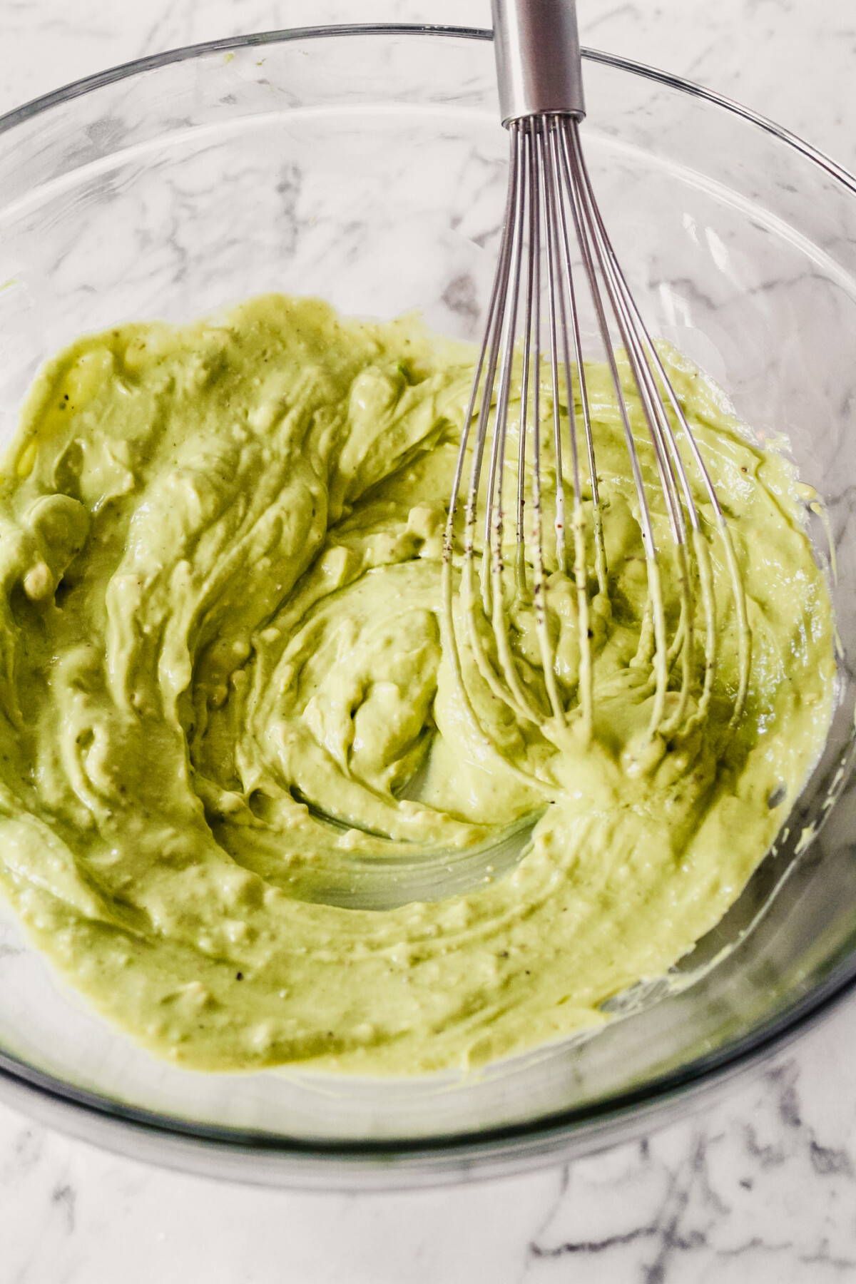 Photograph of an avocado sauce being whisked together in a large glass bowl. 