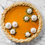 Photography of a pumpkin pie garnished with spiced meringue cookies and pepitas.