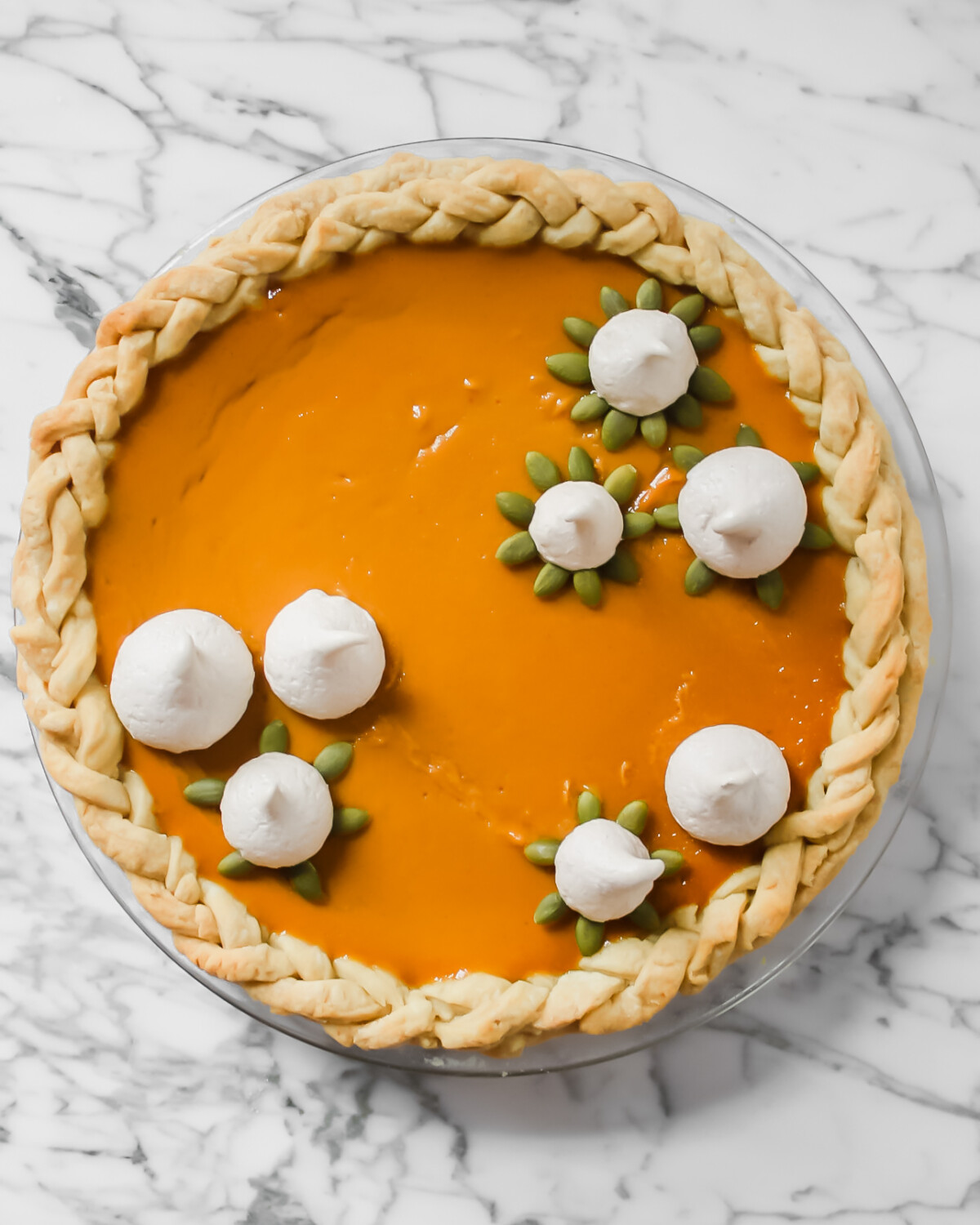 Photography of a pumpkin pie garnished with spiced meringue cookies and pepitas.