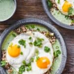 A gray metal plate with green sauce, grains, and sunny side up eggs, set on top of worn wood slabs.