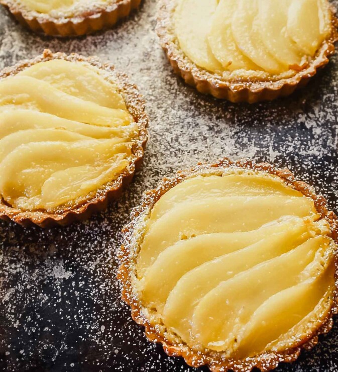 Overhead image of a mini tarts on a balking sheet topped with layered of poaches pears