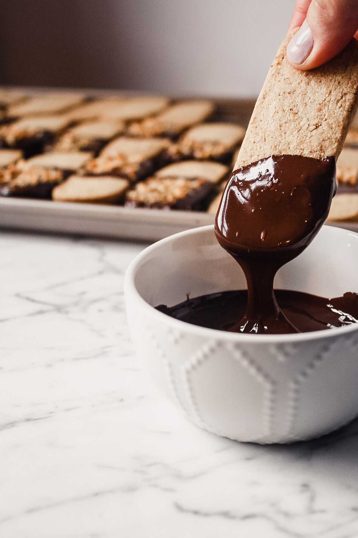 Photograph of shortbread cookie being dunked in melted dark chocolate