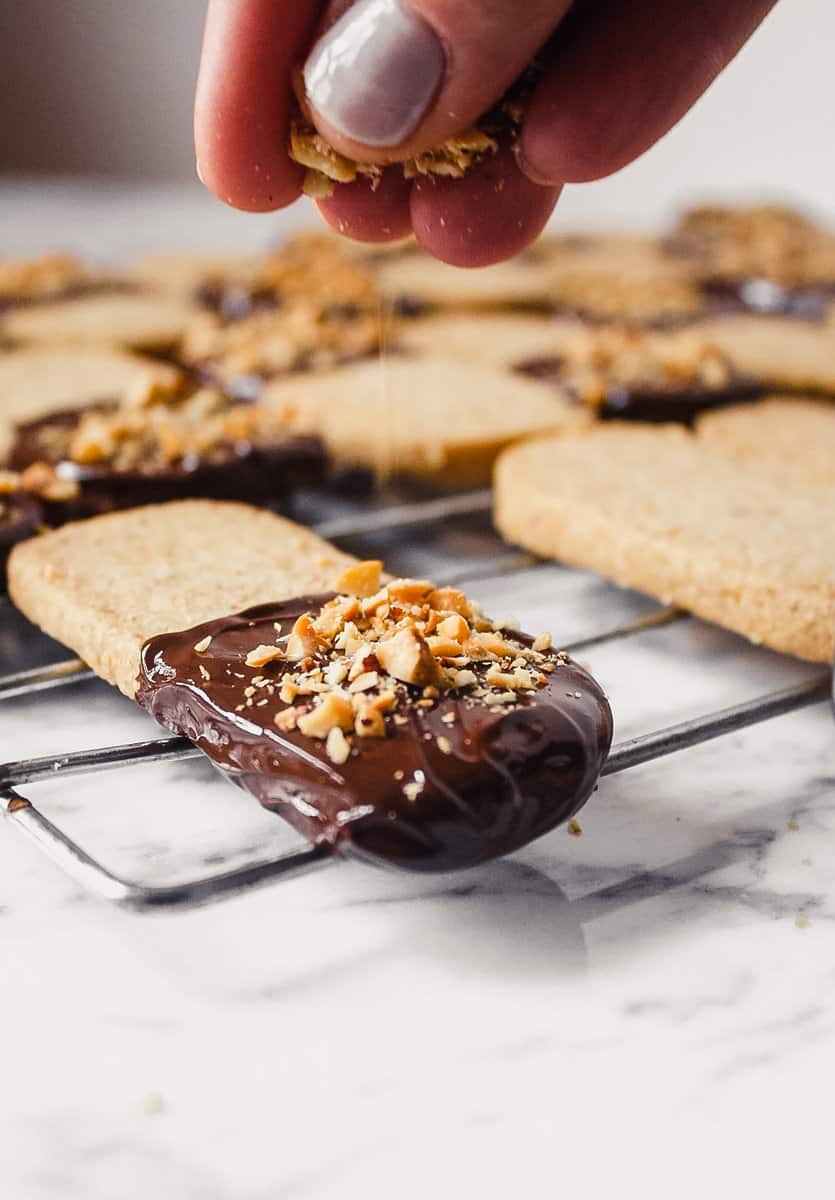 Chocolate dipped shortbread cookies being topped with chopped nuts