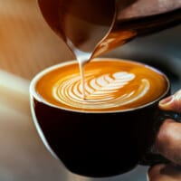 set of hands pouring steamed milk into an espresso mug