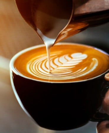 set of hands pouring steamed milk into an espresso mug