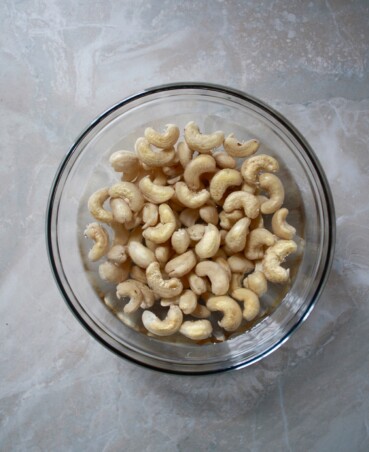 Glass jar filled with water and whole cashews set on a marble surface.