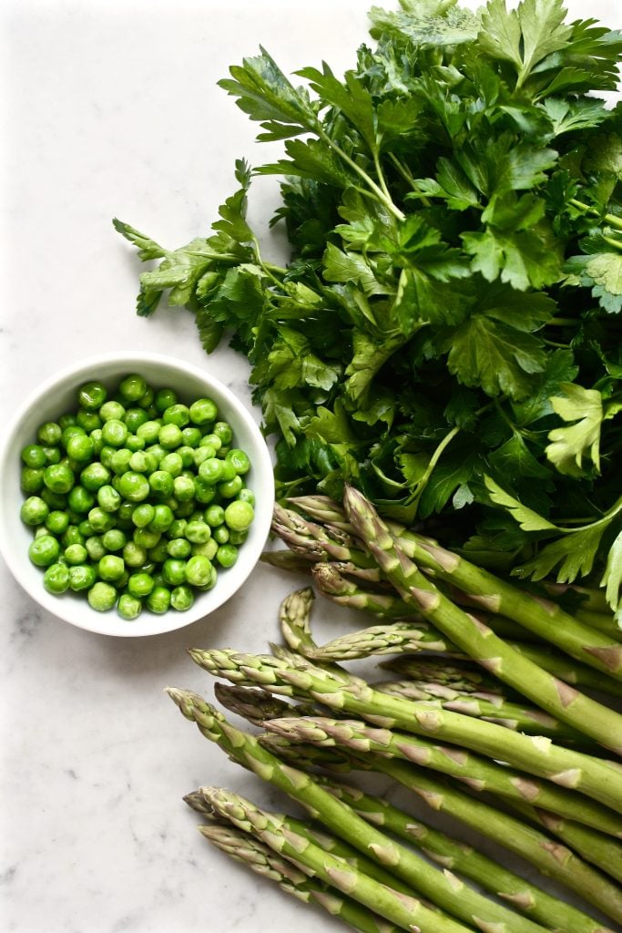 Photograph of asparagus, parsley and peas scattered on a marble table