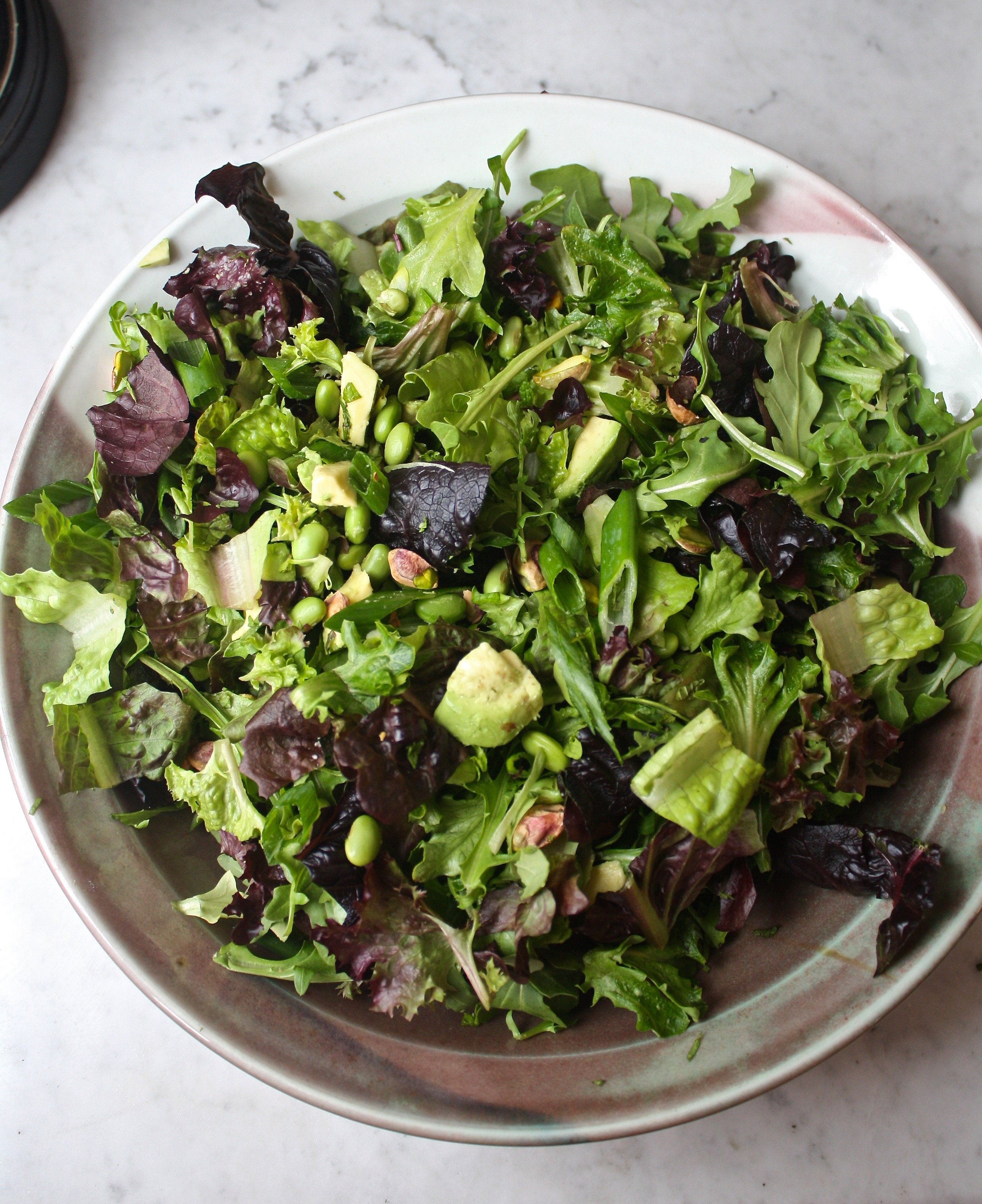 Large green salad in a bowl set on a marble table
