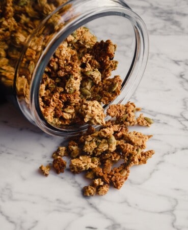 Photograph of granola spilling out of a large glass jar into a marble table