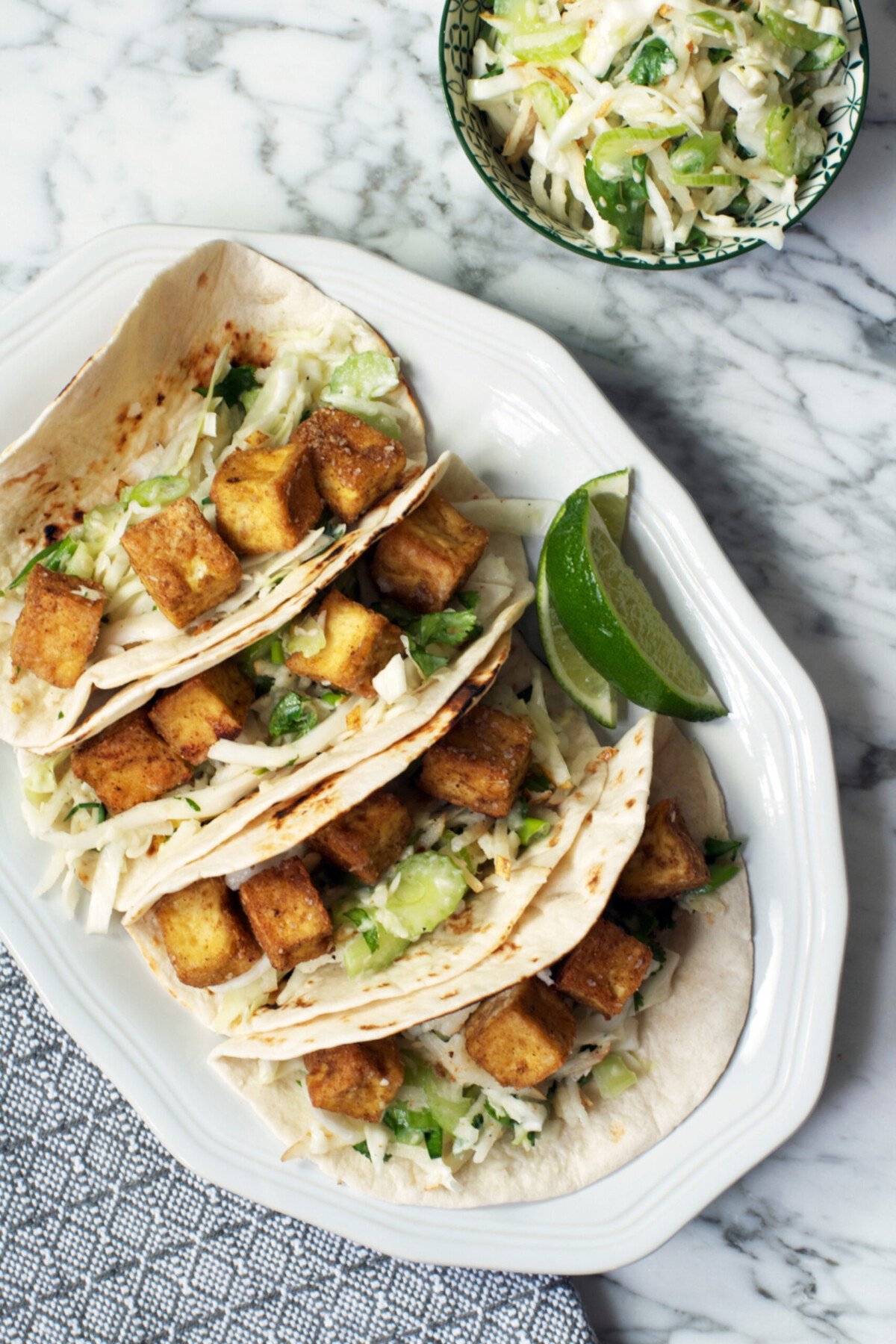 Photograph og tacos filled with crisp tofu and green slaw, arranged on an oval palte