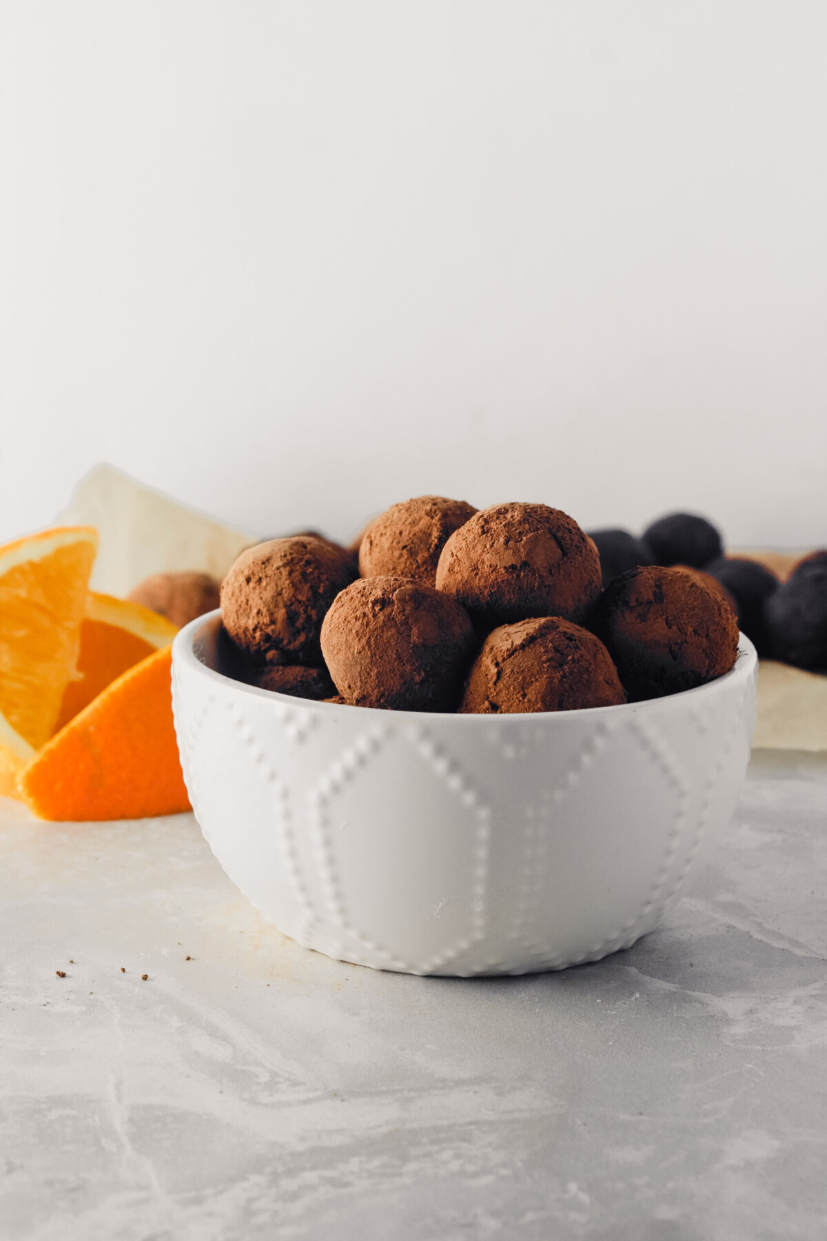 Photograph of vegan dark chocolate truffles stacked in a white bowl, one with a bite taken out of it.