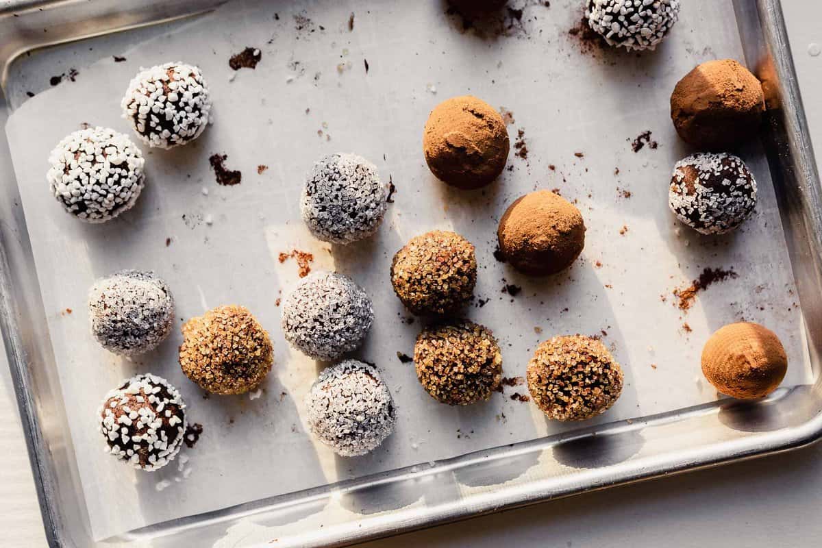 vegan truffles coated in cocoa, sprinkles and sugar arranged on parchment-lined baking sheet