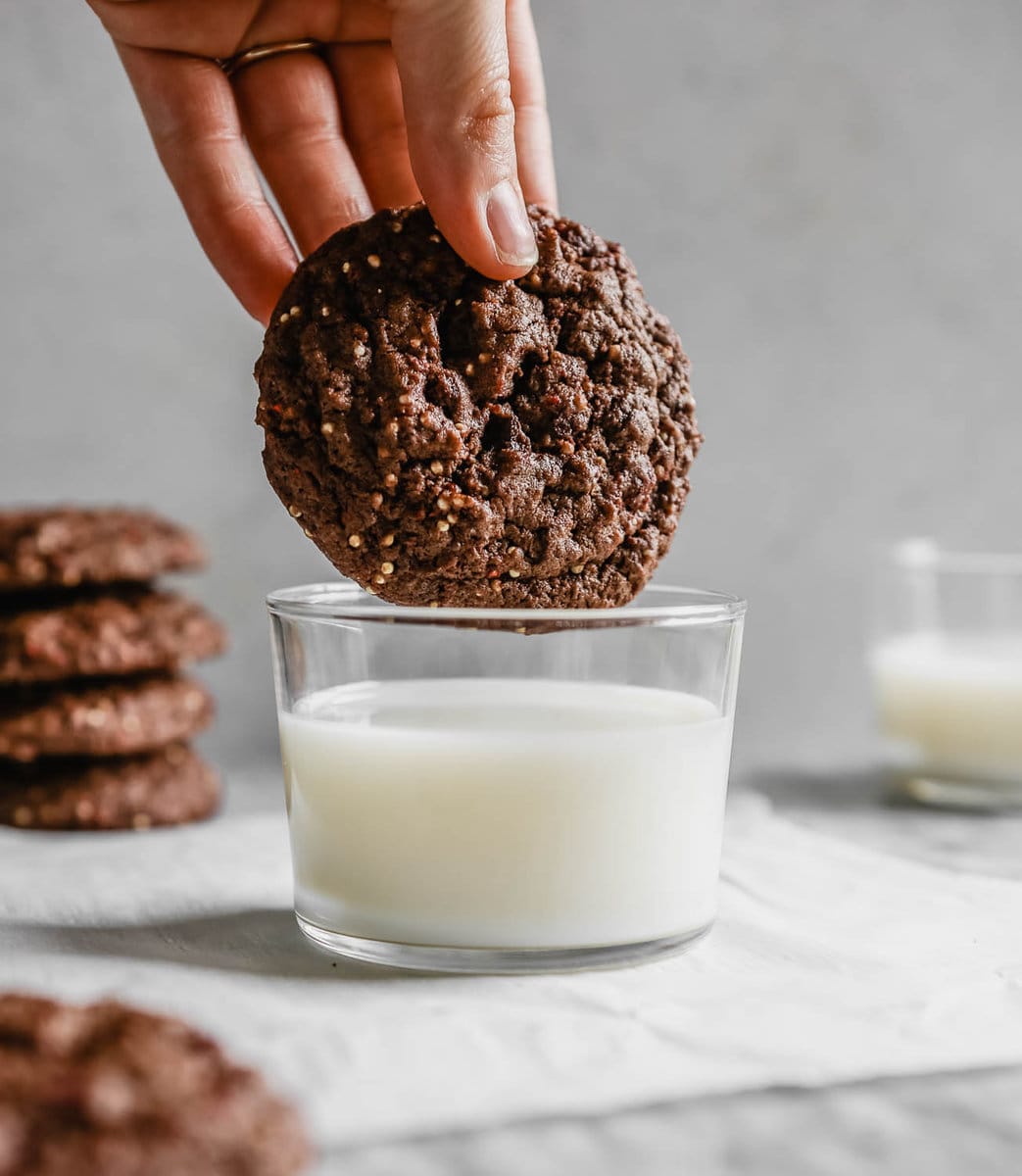 a hand dipping a chocolate cookie in milk