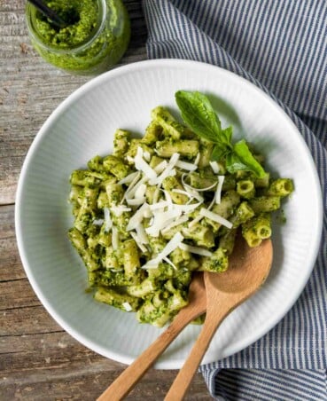 overhead image of pesto pasta in a white bowl set on a wooden table