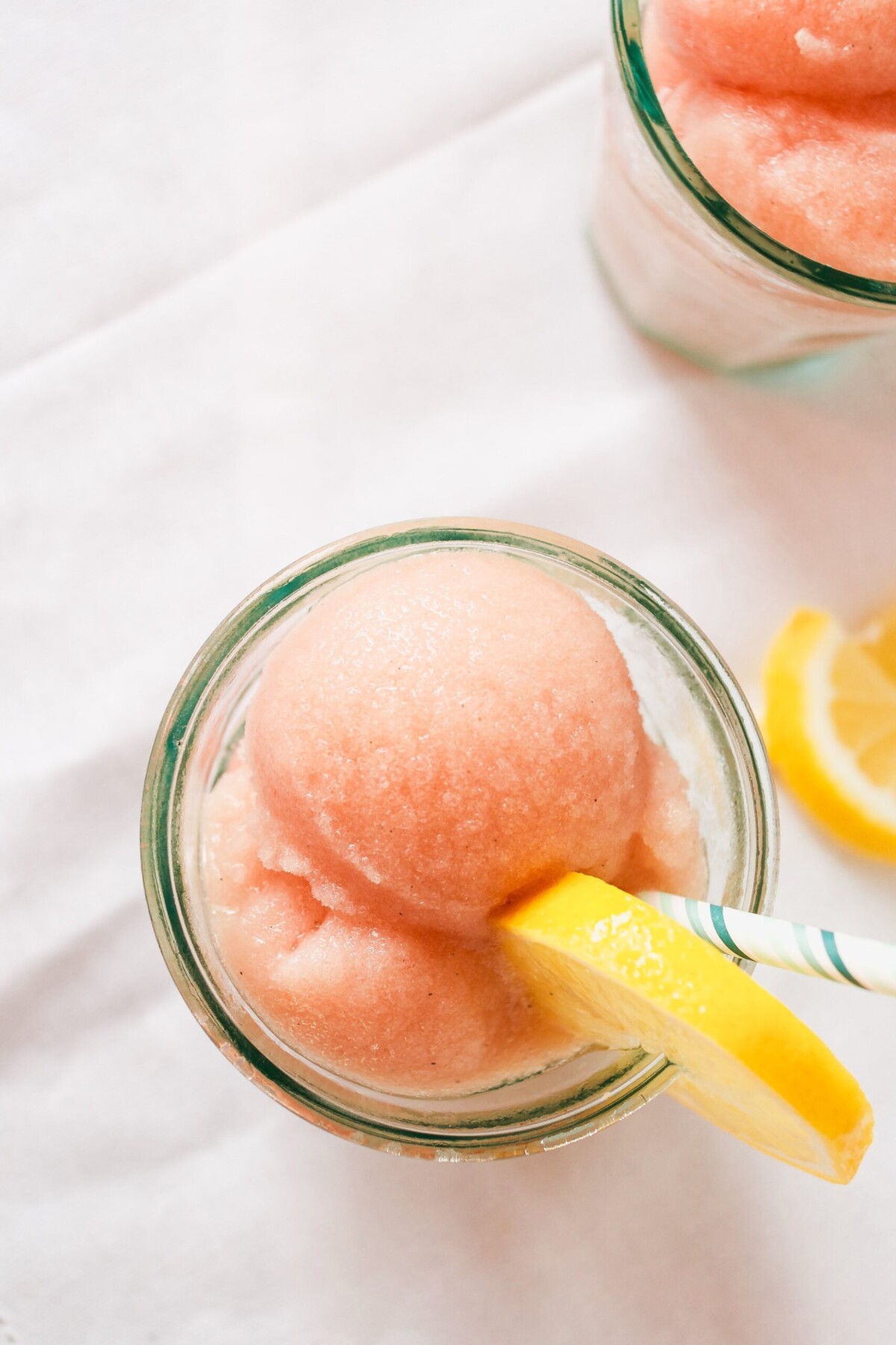 Scoops of rhubarb ice in glasses with lemon slices and spoons. 