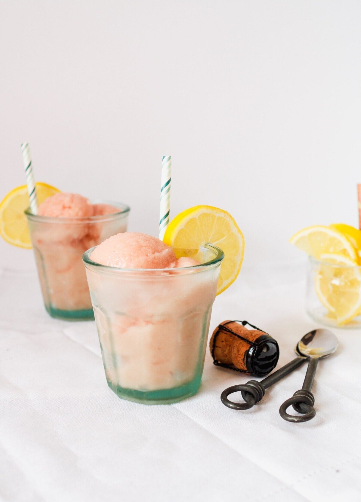 Scoops of rhubarb ice in glasses with lemon slices and spoons. 