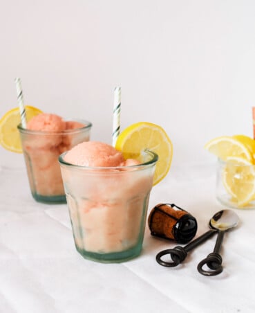 Scoops of rhubarb ice in glasses with lemon slices and spoons.