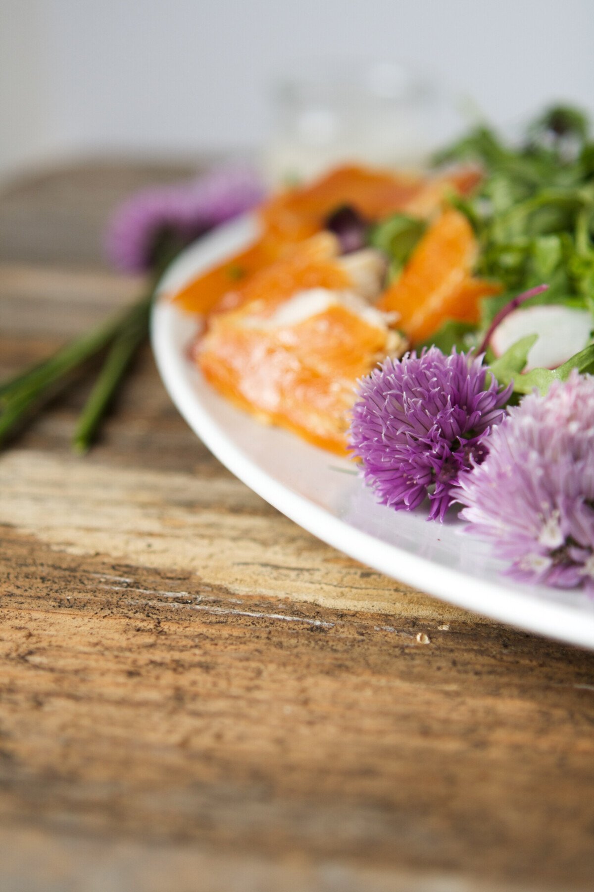 Close up of purple chive blossoms and smoked trout on a white plate