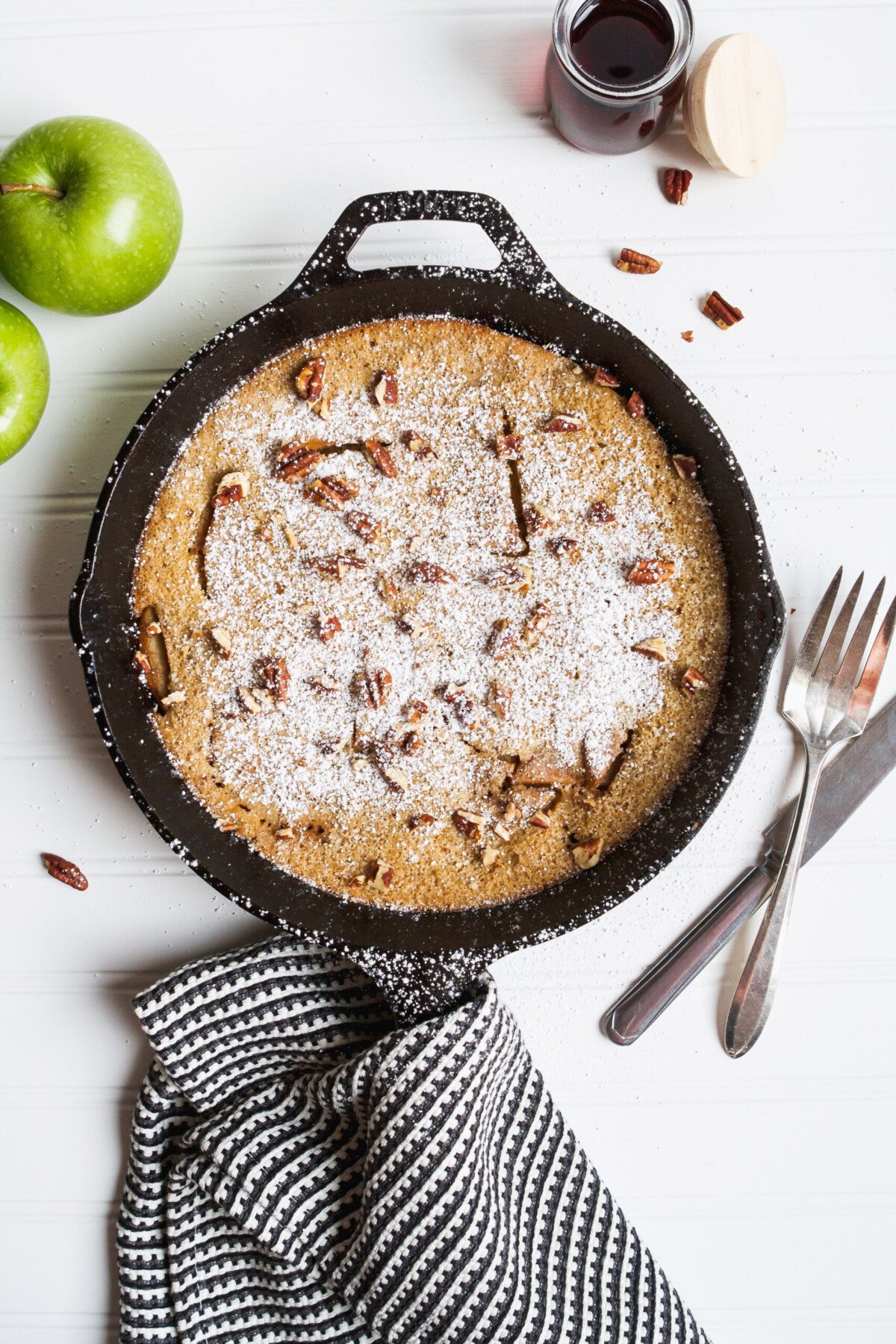 Photograph of a puffed apple pancake in a cast iron skillet on a white table