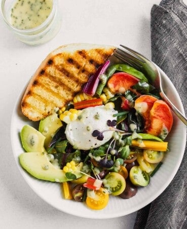 white bowl filled with veggies and fruit, topped with a poached egg and toasted bread