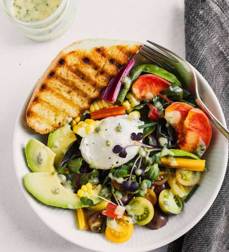 white bowl filled with veggies and fruit, topped with a poached egg and toasted bread