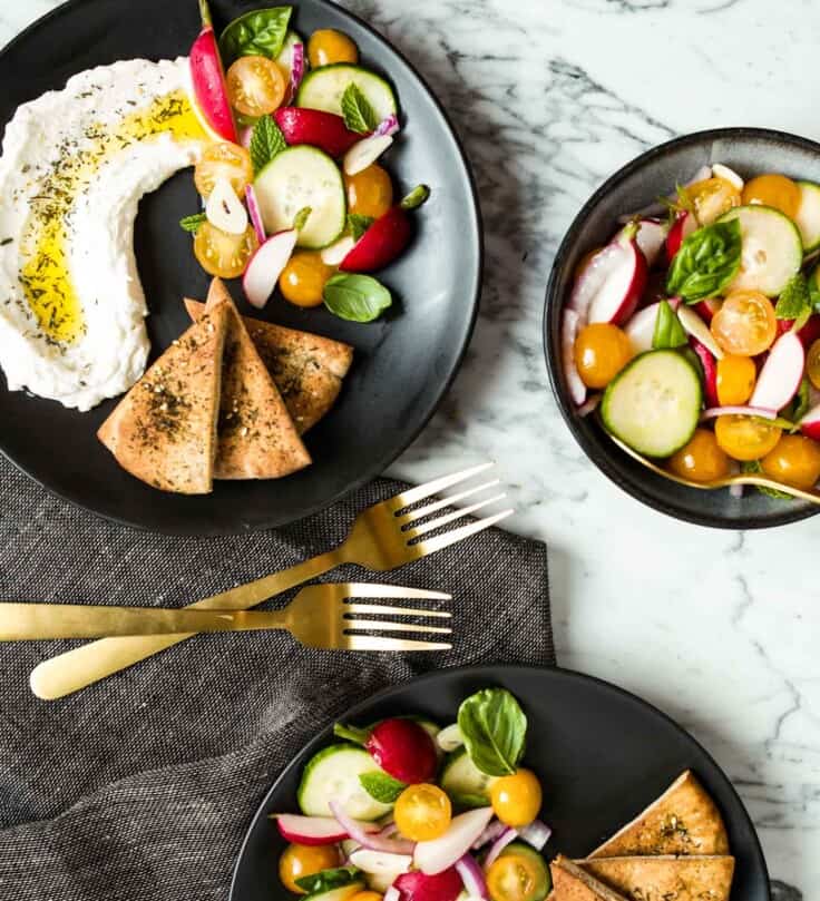 image of vegetables and labneh on a black plate with pita wedges