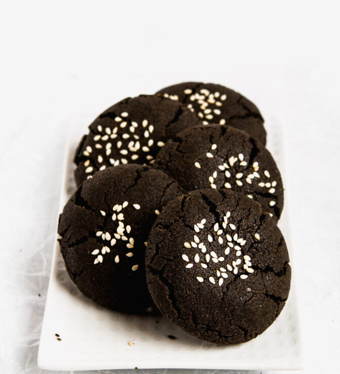 Black tahini cookies stacked on a white plate.