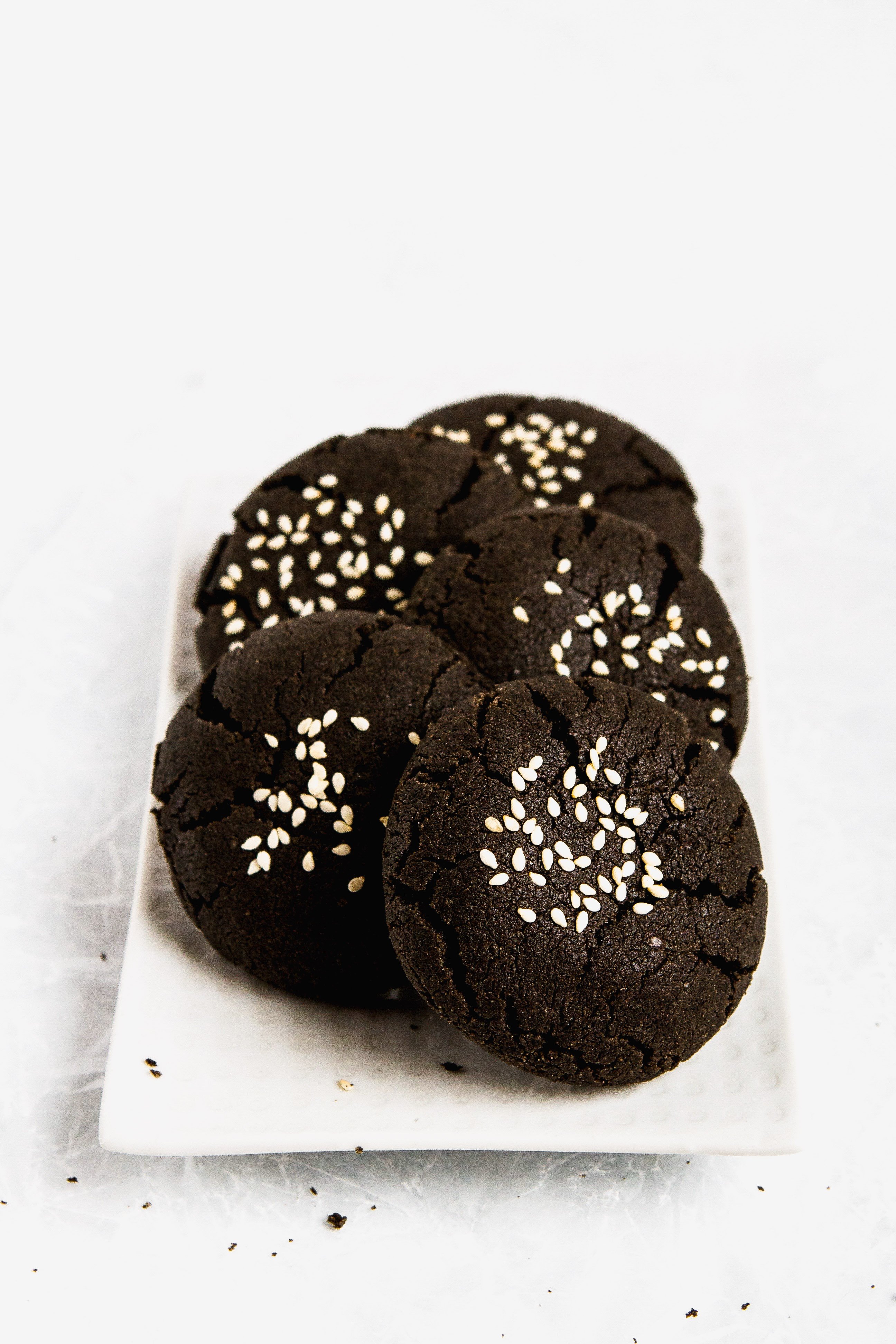 Black tahini cookies stacked on a white plate.