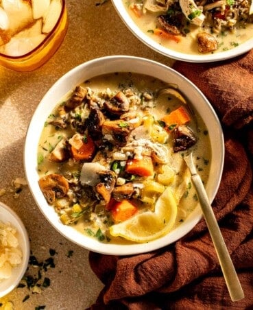 creamy soup with chunks of vegetables and turkey in shallow white bowls with a gold spoon set in them.