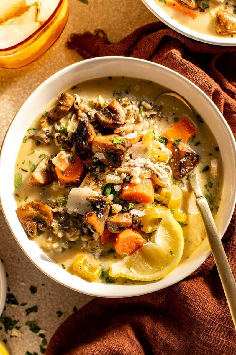 creamy soup with chunks of vegetables and turkey in shallow white bowls with a gold spoon set in them.