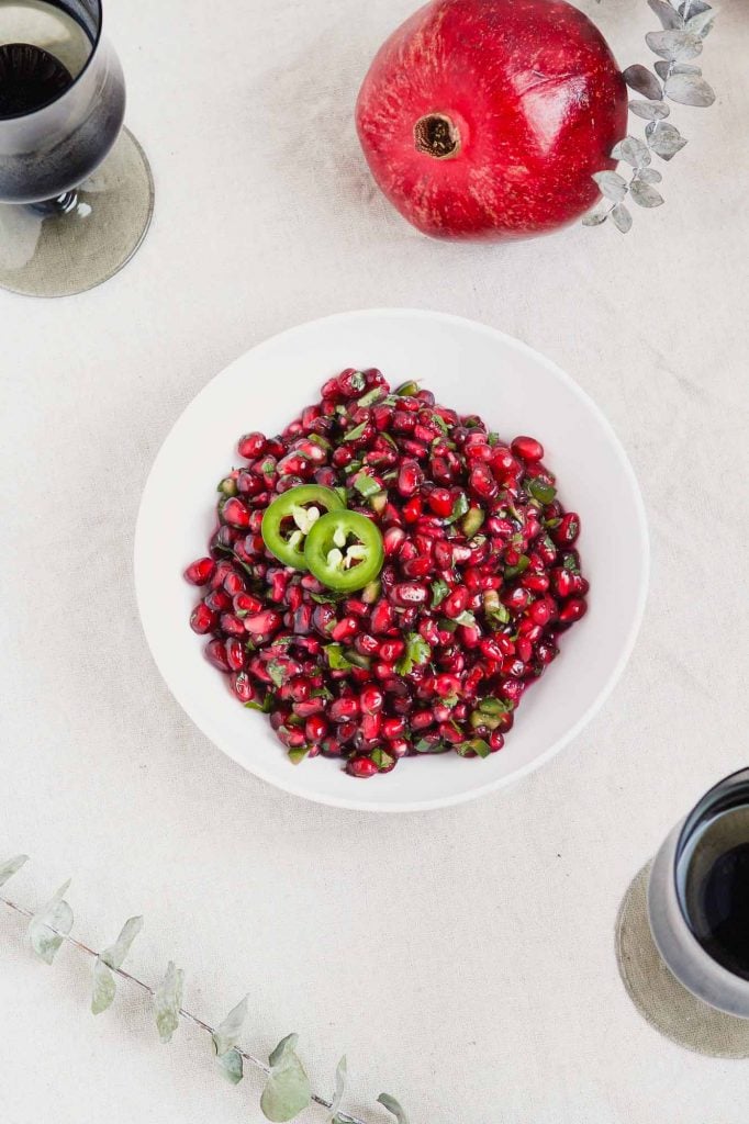 overhead image of pomegranate relish or "salsa" in a white bowl with greens set around it