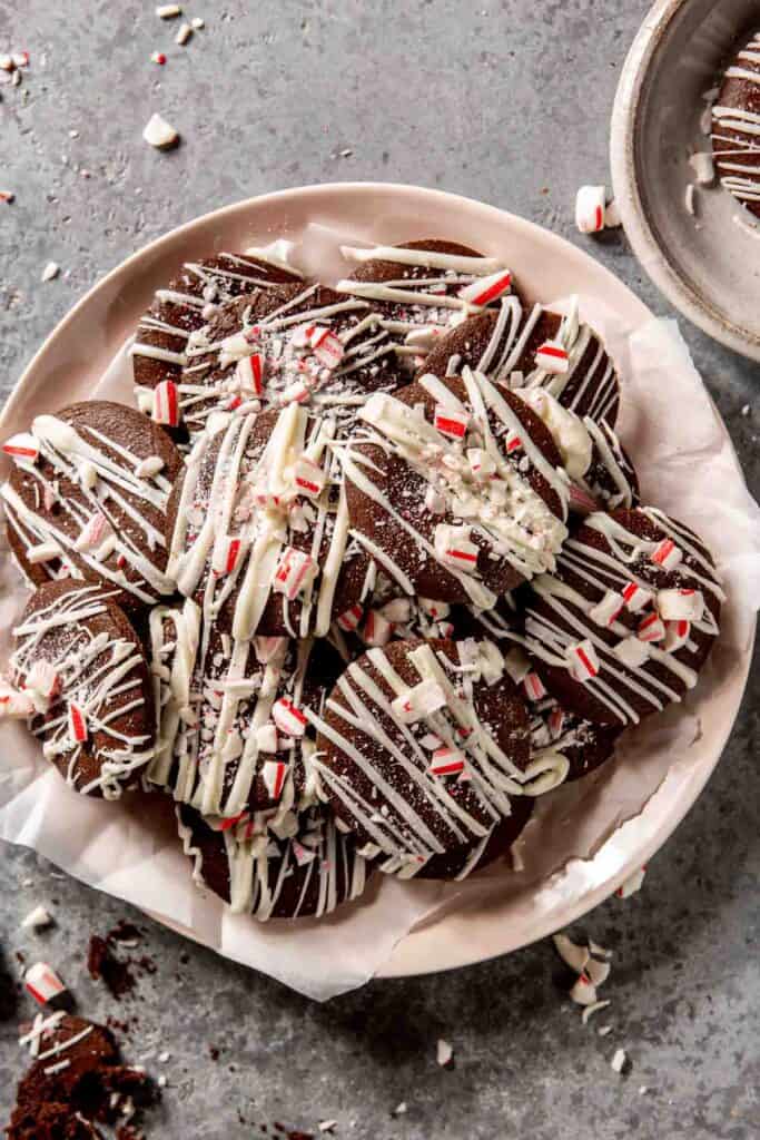 chocolate cookies topped with white chocolate drizzle and crushed peppermint candies set on a parchment-lined plate