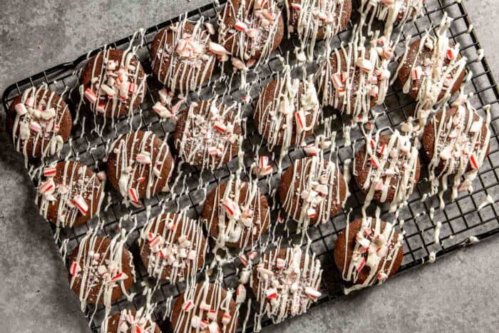 chocolate cookies topped with white chocolate drizzle and crushed peppermint candies set on a wire rack