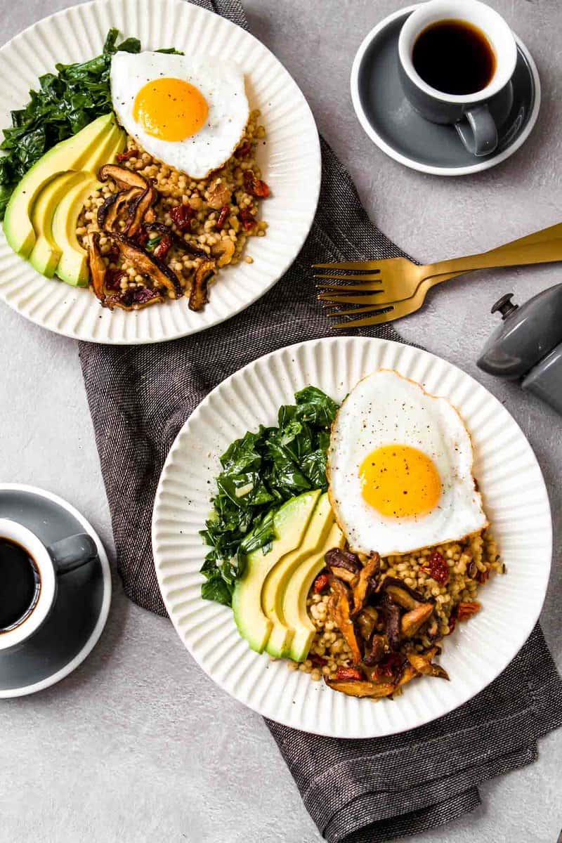 overhead image of cream-colored bowls piled high with sorghum, cooked greens, crispy mushrooms, an egg and avocado