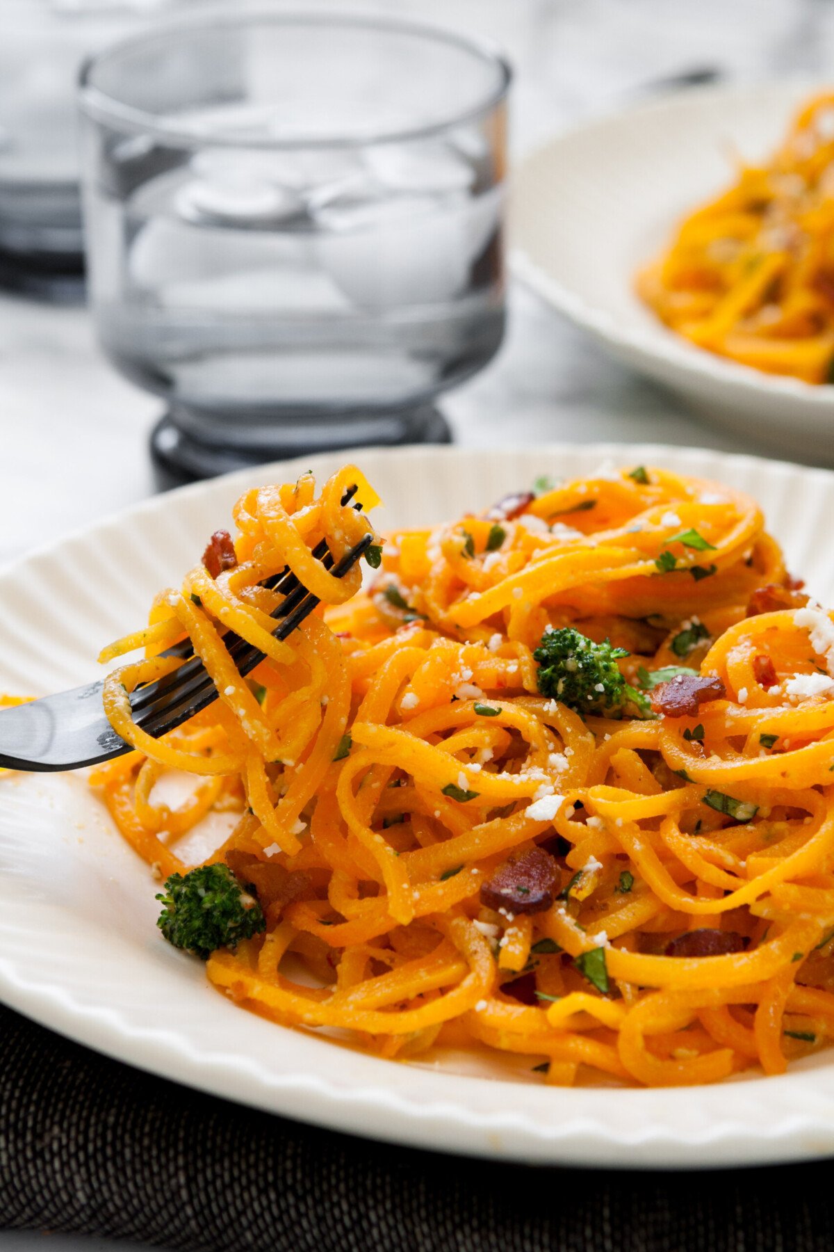 Butternut squash noodles spun around a black fork with broccoli and bacon